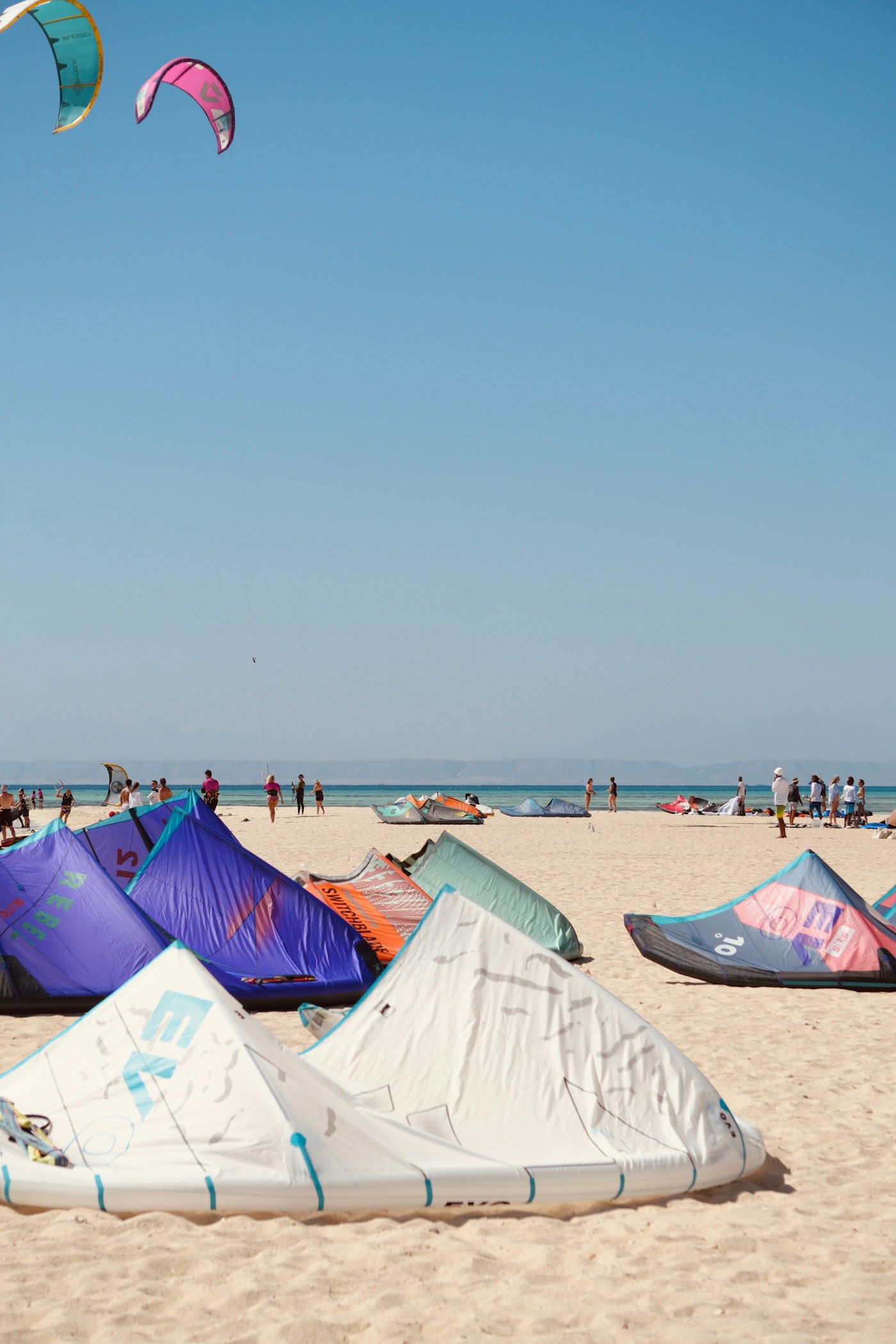 Kitesurf equipment and riders on a sandy beach